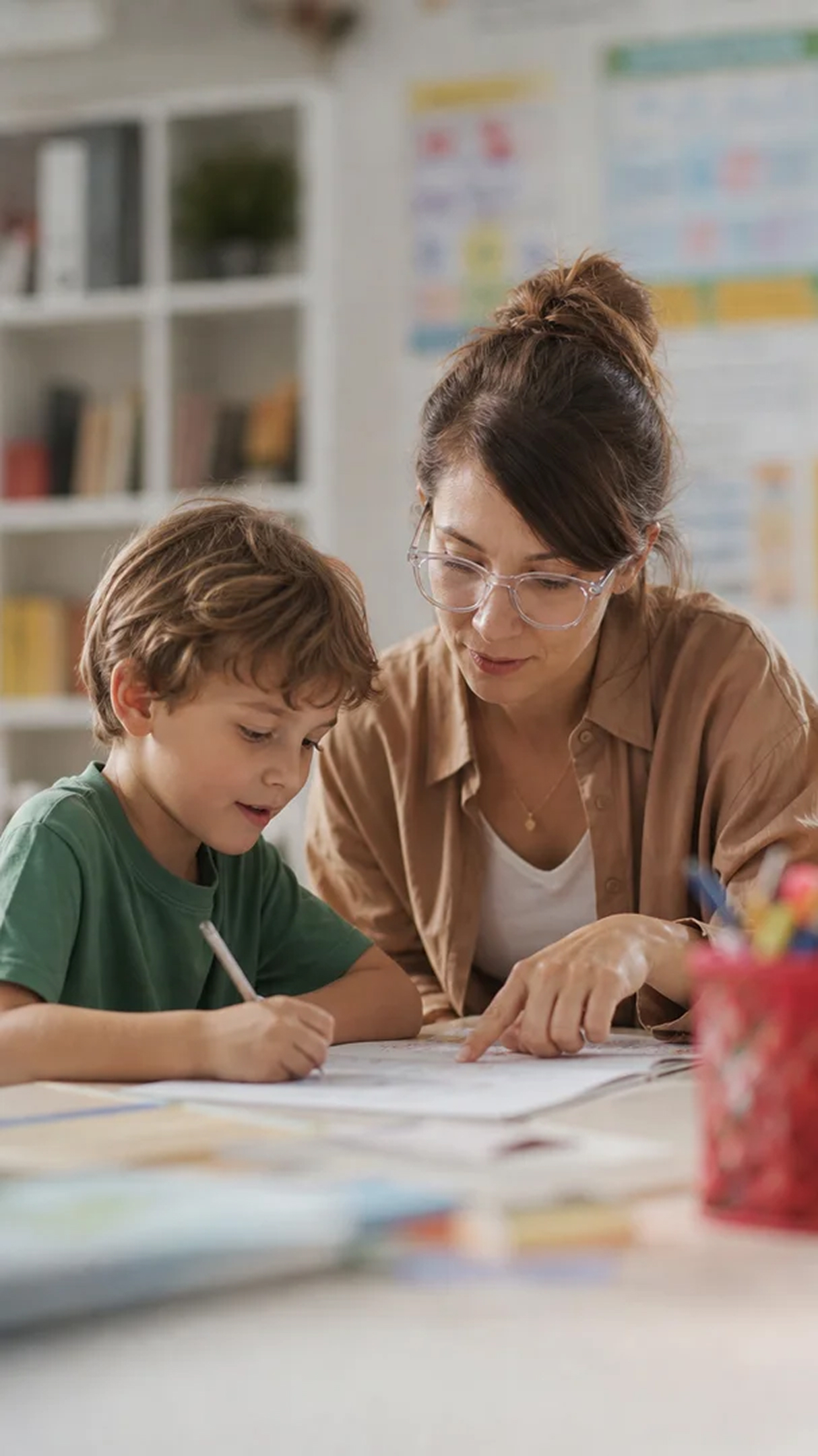 Adult helping a child with schoolwork at a table.